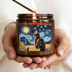 Peut inclure: Une bougie en pot de verre brun avec une mèche allumée, portant une étiquette illustrée d'un chat sous un ciel étoilé. Le texte sur l'étiquette indique Hand-Poured Coconut Soy Wax et Fragrance: Blackberry Vanilla dans une police lisible.