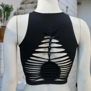 May include: Black sleeveless crop top with a unique criss-cross design on the back. The design features multiple cutouts and a woven pattern.