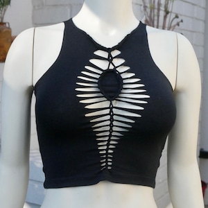 May include: A black crop top with a unique cut-out design featuring a braided pattern and a circular opening at the center.