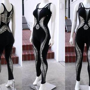 May include: Black one-piece jumpsuit with a cut-out design. The jumpsuit has a scoop neck and sleeveless straps. The cut-outs are in a geometric pattern and extend from the shoulders to the legs.