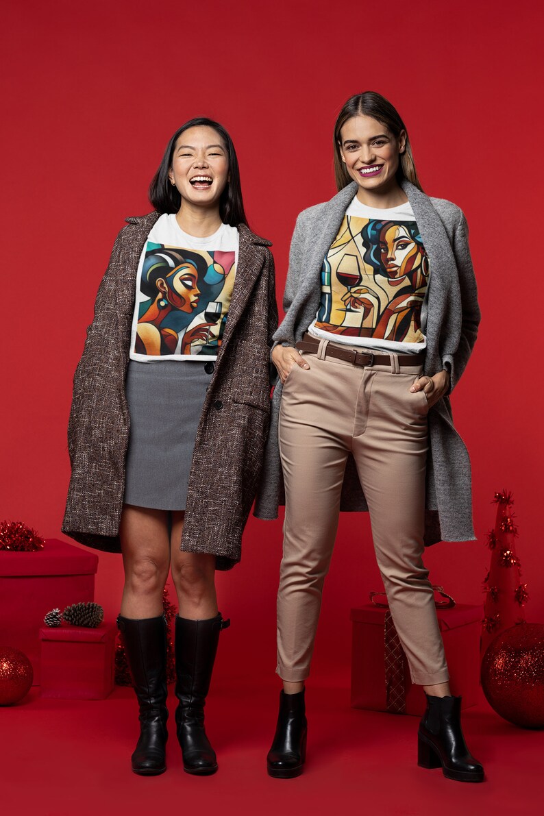May include: Two people wearing white t-shirts with a colorful abstract design of a woman holding a glass of wine. The person on the left is wearing a brown tweed coat and a gray skirt. The person on the right is wearing a gray cardigan and beige pants. Both are wearing black boots. The background is a solid red.