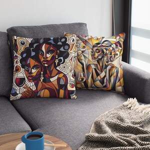 May include: Two throw pillows with abstract art featuring women with colorful geometric patterns and a glass of wine. The pillows are on a gray couch with a blanket.