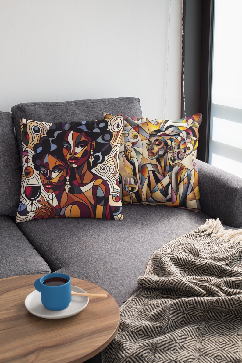 May include: Two throw pillows with abstract art featuring women with colorful geometric patterns and a glass of wine. The pillows are on a gray couch with a blanket.