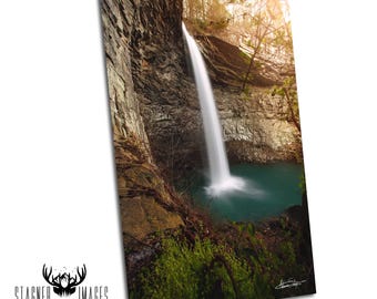 Peut inclure: Une impression photographique verticale représentant une cascade dévalant une falaise rocheuse texturée et accidentée dans un bassin bleu sarcelle profond. La scène comprend des arbres dénudés, du feuillage vert et une lumière chaude.