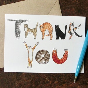 Pu&ograve; includere: Un biglietto bianco con la parola "GRAZIE" scritta usando illustrazioni di gatti in varie pose. I gatti sono disegnati in uno stile cartone animato e sono di diversi colori, tra cui nero, bianco, arancione e marrone.