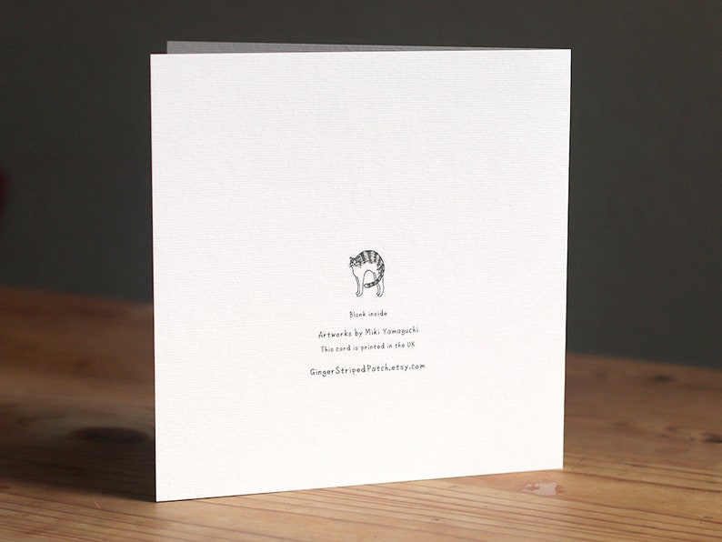 May include: A white card with a black and white illustration of a cat on the back. The text on the back reads "Blank inside", "Artwork by Miki Yamaguchi", "This card is printed in the UK", and "GingerStripedPatch.etsy.com".