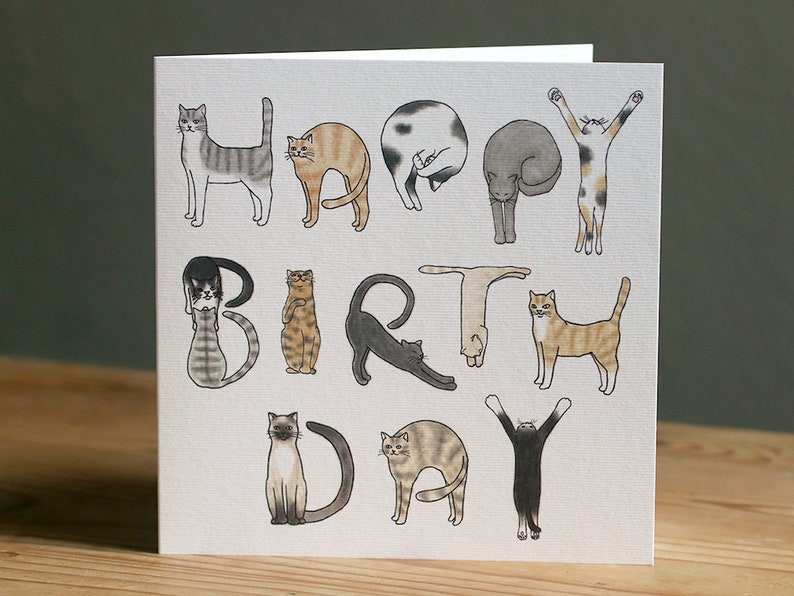 May include: A greeting card with the words "Happy Birthday" spelled out using illustrations of cats in different poses. The cats are drawn in a simple, cartoon style and are colored in shades of brown, gray, black, and white.