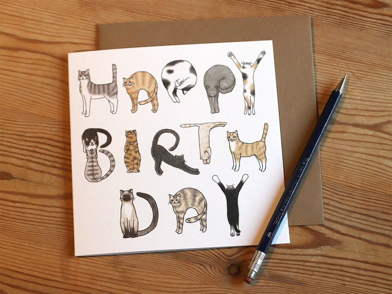 May include: A white card with a birthday greeting spelled out using illustrations of cats. The greeting reads "Happy Birthday".