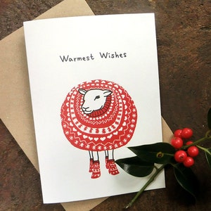 May include: A white sheep wearing a red and white knitted sweater with a red scarf and red boots. The card says "Warmest Wishes".