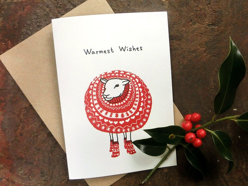 May include: A white sheep wearing a red and white knitted sweater with a red scarf and red boots. The card says "Warmest Wishes".