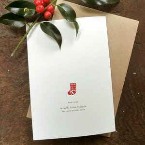 May include: A blank white card with a red and white Christmas stocking illustration. The text on the card reads "Blank inside" and "Artwork by Miki Yamaguchi. This card is printed in the UK."