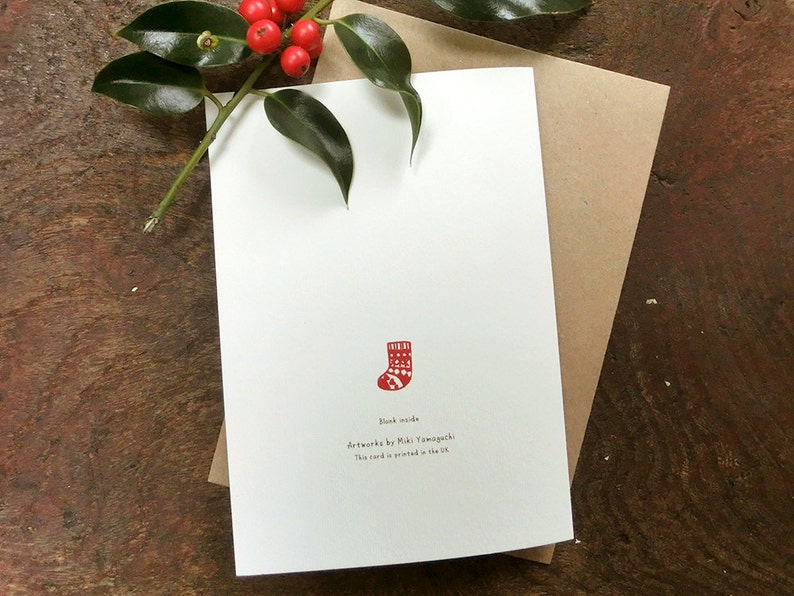May include: A blank white card with a red and white Christmas stocking illustration. The text on the card reads "Blank inside" and "Artwork by Miki Yamaguchi. This card is printed in the UK."