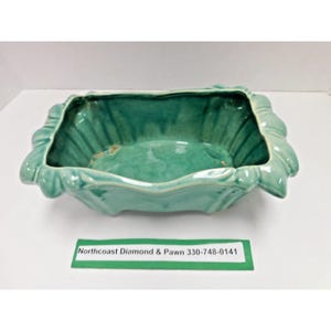 May include: A rectangular ceramic planter with a glossy teal glaze and a scalloped, fluted rim. The interior features a smooth basin with subtle color variations. A green rectangular label with the text Northcoast Diamond & Pawn 330-748-0141 is placed in front of the ceramic vessel.