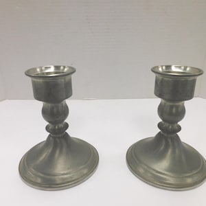 May include: A white ceramic mug with a black handle and the text "But First, Coffee" in a black, handwritten-style font. The mug is on a white surface.