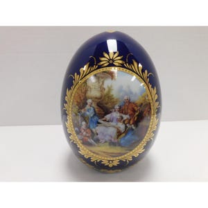 May include: A cobalt blue decorative egg with a gold floral design and a painted scene of people in a garden. The egg has a glossy finish and is a decorative item.