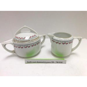 May include: A white porcelain sugar bowl with a lid and a matching creamer, both featuring a delicate floral pattern of pink roses and green leaves with gold trim. A small rectangular sign reads North coast diamond & pawn 330 - 748-0141.