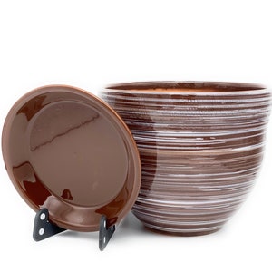 May include: A brown ceramic planter with a white striped design and a matching saucer. The planter is round and has a wide opening.