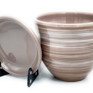 May include: A brown ceramic planter with a white striped design. The planter has a matching saucer.