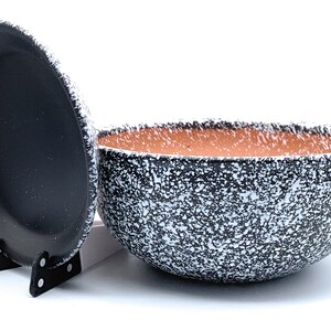 May include: A black and white speckled ceramic bowl with a matching lid. The bowl has a brown terracotta rim.