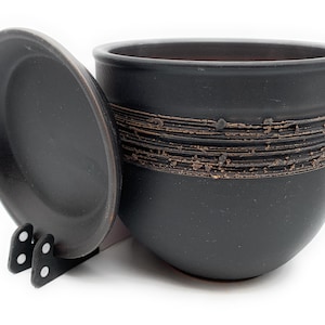 May include: Black ceramic planter with a lid. The planter has a decorative band of brown and black around the middle.