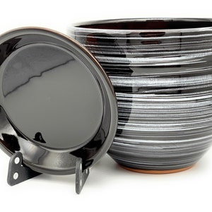 May include: Black and white striped ceramic planter with a matching lid. The planter has a rounded shape and a slightly flared rim. The lid has a smooth, flat surface.