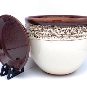 May include: A white ceramic planter with a brown rim and a brown speckled band around the middle. The planter comes with a matching brown saucer.