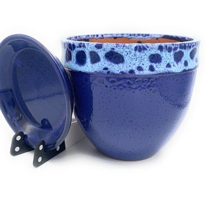 May include: A blue ceramic planter with a white and blue speckled rim and a matching lid. The planter is sitting on a white surface.