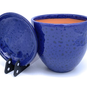 May include: A blue ceramic pot with a matching lid. The pot has a speckled glaze and a rounded shape.