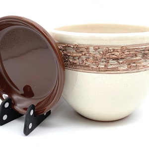 May include: A white ceramic planter with a brown textured band around the middle. The planter comes with a matching brown saucer.