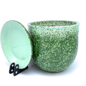 May include: A green ceramic planter with a speckled glaze. The planter has a matching lid and is sitting on a white surface.