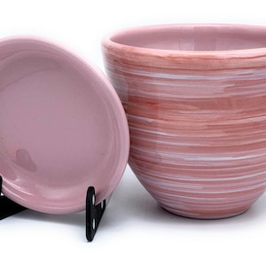May include: A set of two pink ceramic planters with a white swirl design. The larger planter is taller and wider than the smaller planter. Both planters have a smooth, glossy finish.