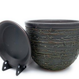 May include: A dark brown and green ceramic planter with a textured finish. The planter has a matching saucer.