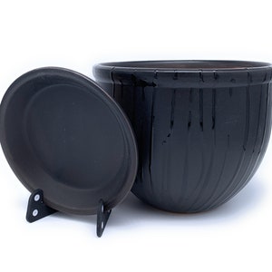 May include: Black ceramic planter with a matching saucer. The planter has a textured, wood-like design.