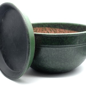 May include: A green ceramic bowl with a matching saucer. The bowl has a speckled finish and a dark green exterior with a reddish-brown interior. The saucer is dark green and slightly angled.