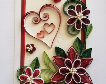 Könnte beinhalten: Eine handgemachte Grußkarte mit einem Papierquilling-Design in Rot, Weiß und Grün. Das Design beinhaltet ein großes Herz mit zwei kleineren Herzen darin und drei Blumen mit weißen Zentren.