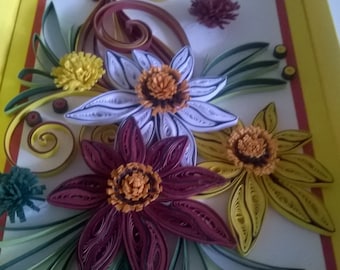 May include: A framed paper craft featuring a bouquet of flowers made from curled paper. The flowers are in shades of white, yellow, red, and green. The frame is yellow with a red and yellow border.