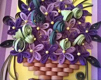 May include: A purple and green paper flower arrangement in a brown basket. The flowers are made of curled paper and are arranged in a basket made of brown paper. The background is a yellow and purple card.