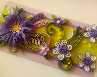 May include: A handmade card with a purple and white paper flower design. The card features a large purple flower with a yellow center, surrounded by smaller white and purple flowers. The background is a light green with purple stripes.