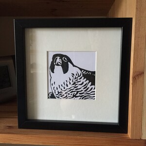 May include: A black and white framed print of a stylized illustration of a falcon with its head tilted up.