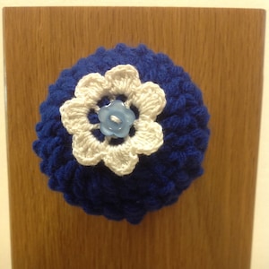 May include: A blue crocheted flower with a white crocheted flower on top and a blue button in the center.