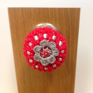 May include: A red and silver crocheted flower door knob cover.