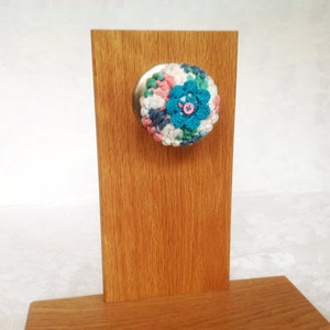 May include: A crocheted door knob cover in shades of pink, blue, green, and white with a blue button in the center.