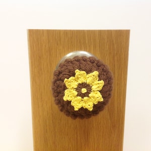 May include: A brown crocheted door knob cover with a yellow crocheted flower in the center.