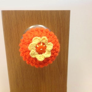 May include: Orange crocheted door knob cover with a yellow crocheted flower and a red button in the center.