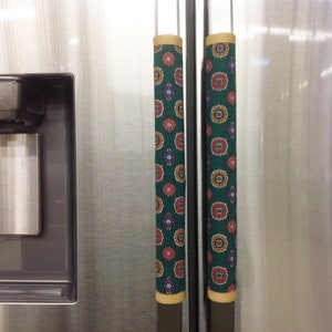 May include: Two green fabric refrigerator handle covers with a colorful geometric pattern. The covers have a yellow trim.