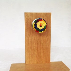 May include: A colorful crocheted flower door knob cover with a yellow center and red bead in the center. The cover is attached to a silver door knob.