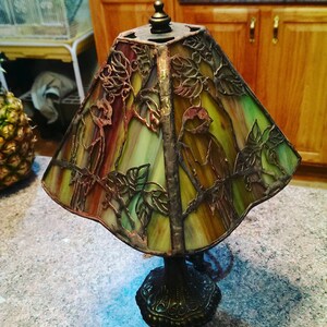 May include: A stained glass lamp with a bronze base and a design of birds and leaves. The lampshade is green, brown, and red.