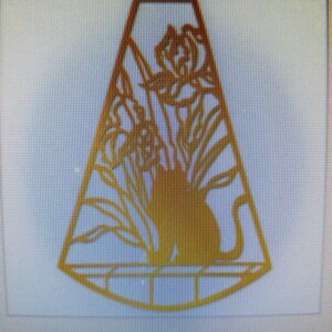 May include: A gold-colored metal silhouette of a cat sitting in a window with flowers outside. The cat is facing to the right and the flowers are on the left side of the image. The silhouette is cut out of the metal and has a delicate design.