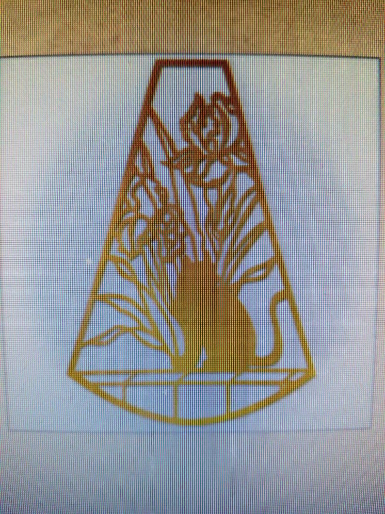 May include: A gold-colored metal silhouette of a cat sitting in a window with flowers outside. The cat is facing to the right and the flowers are on the left side of the image. The silhouette is cut out of the metal and has a delicate design.