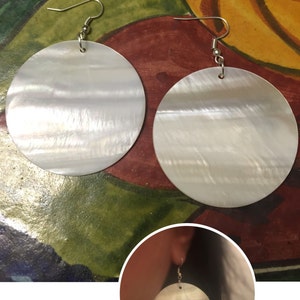 May include: A pair of white shell earrings with silver hooks. The earrings are round and have a pearlescent finish.